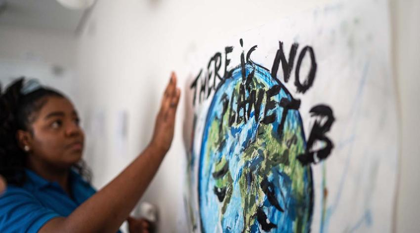 A young woman looks at a piece of art on a wall that reads "There is No Planet B"