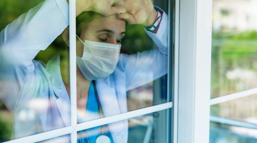 Worried female doctor with arms raised and leaning in the hospital window