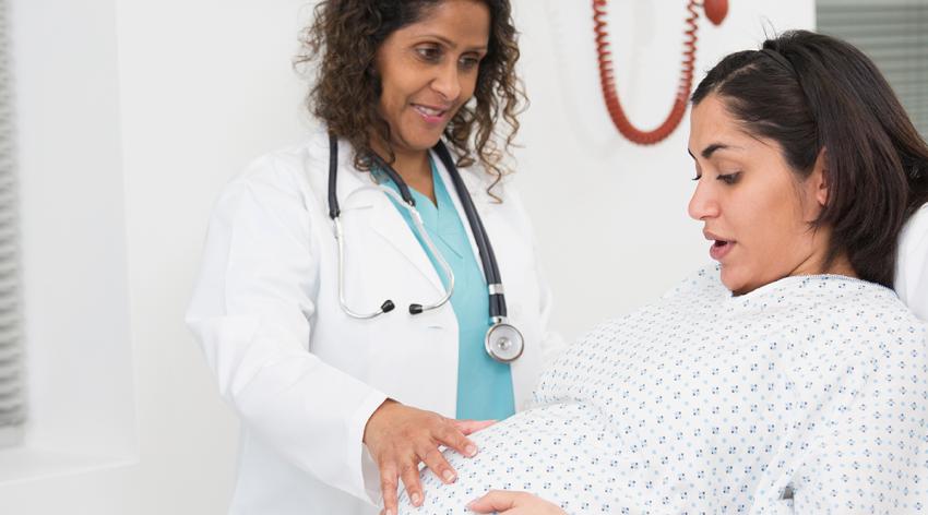 Mixed race doctor examining pregnant patient’s belly