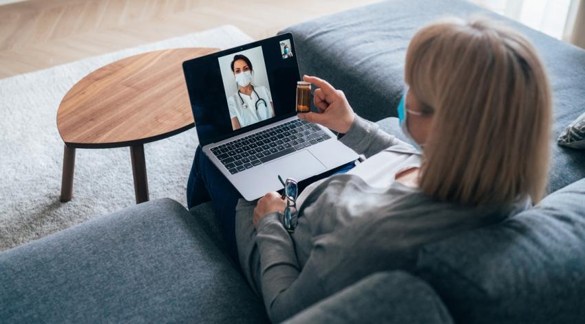 A woman video chats with her doctor while both wear face masks.