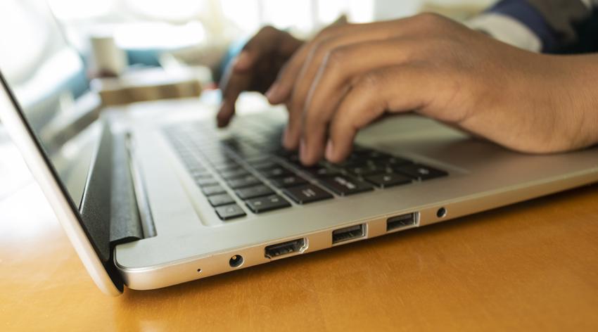 A close-up image of a persons hands typing on a laptop