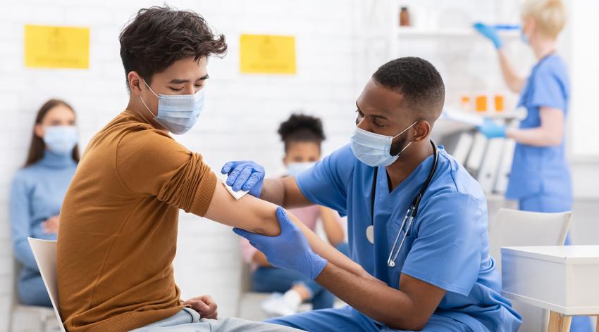 A patient receives a vaccine from a medical professional while others wait in the background