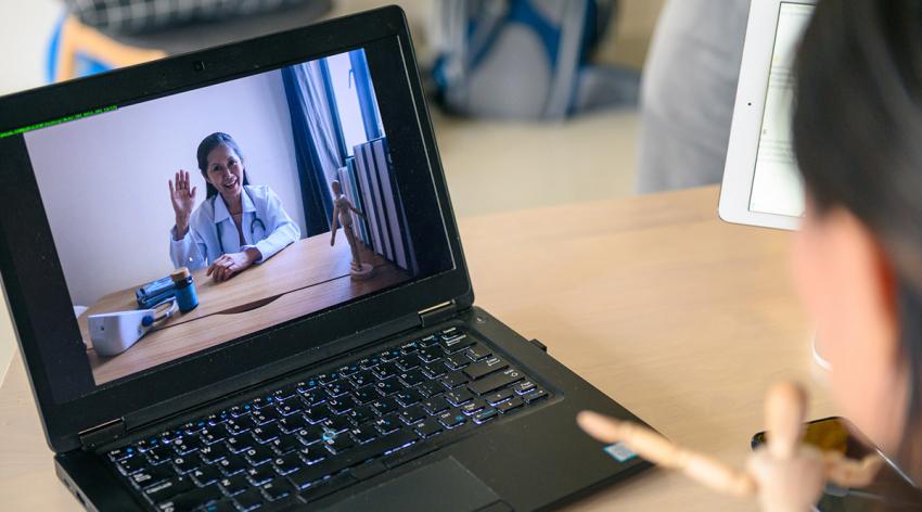 A person in a white coat appears on the screen of a laptop