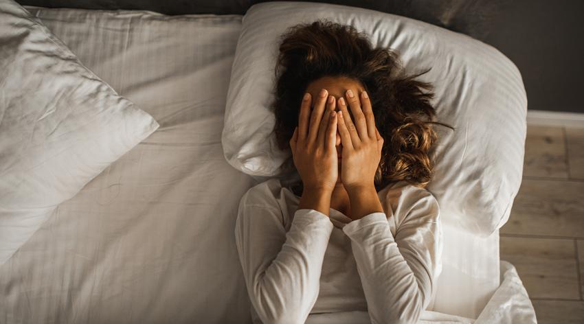 Woman closed face with hands in bed