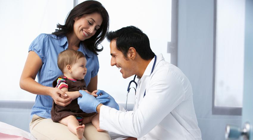 Doctor examining baby girl with mother smiling