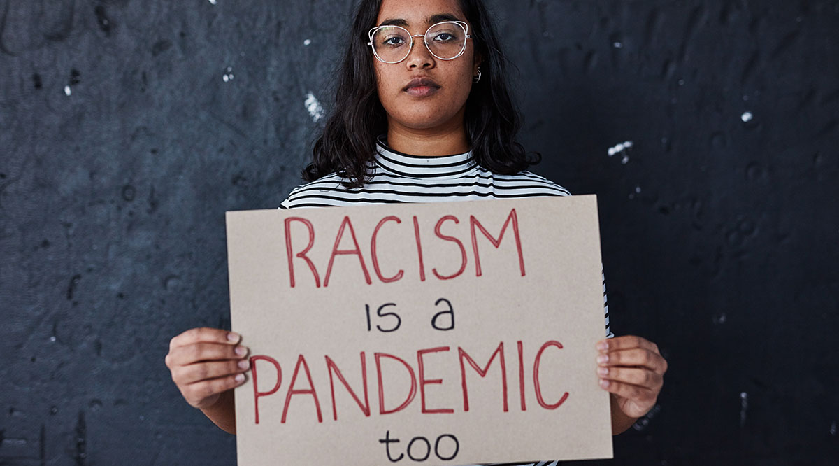 Woman holding a sign saying "Racism is a pandemic too"
