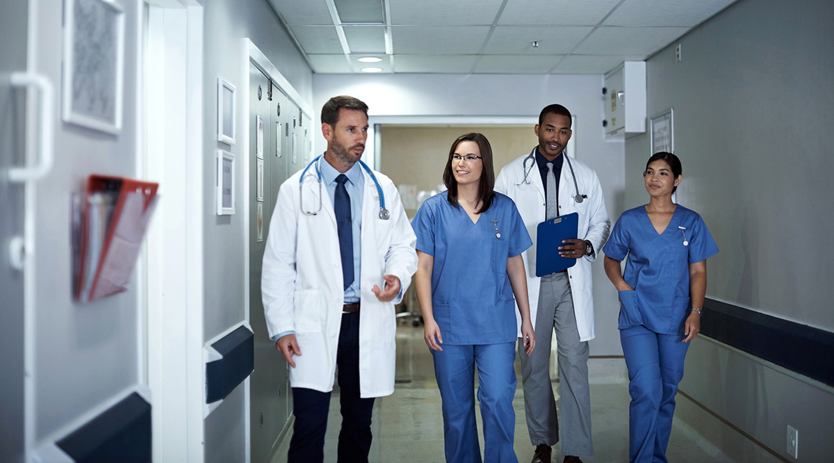 A group of male and female colleagues walk down a hospital hallway. 