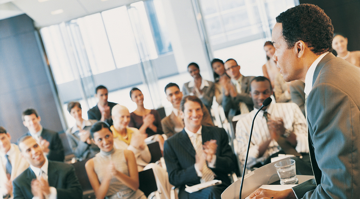 Businessman standing at a podium and giving a speech to a conference room full of delegates