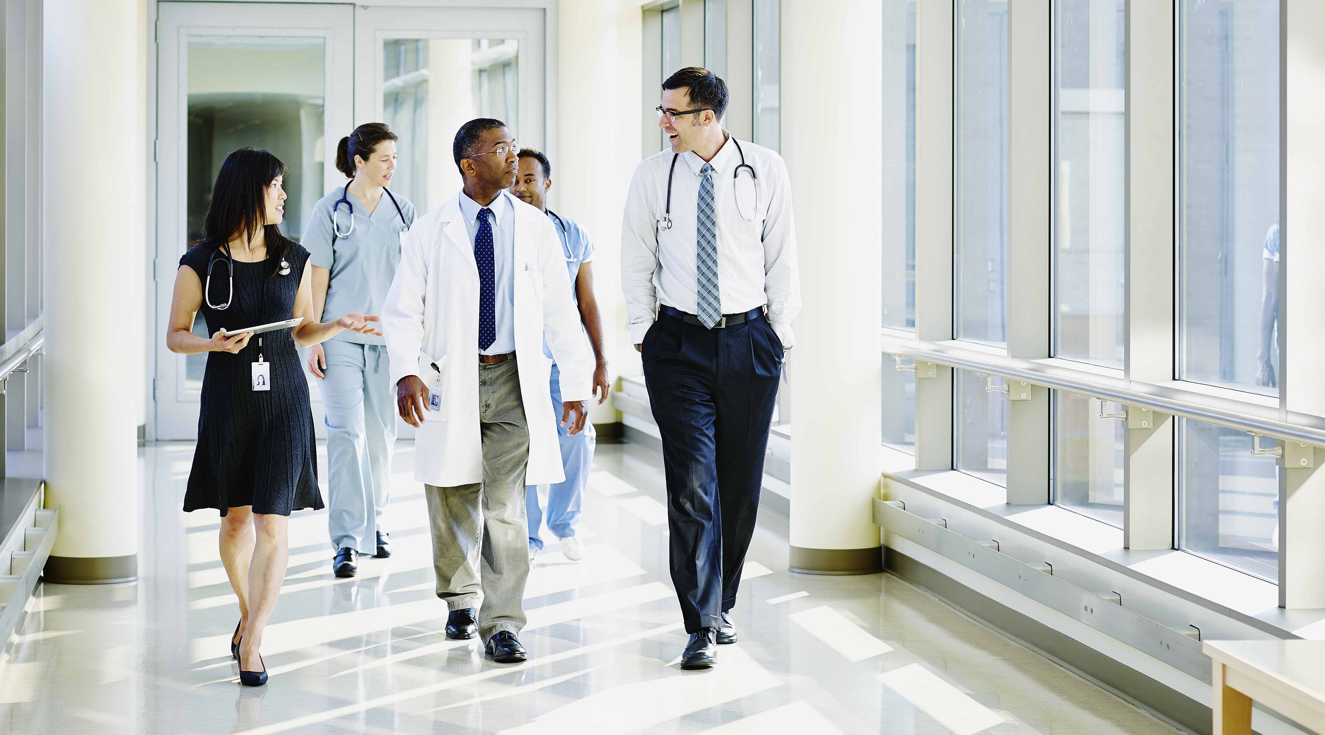 A group of doctors have a conversation while walking down a hallway.