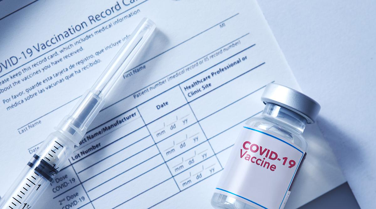 A vial of coronavirus vaccine on a vaccination record card with a syringe on the side