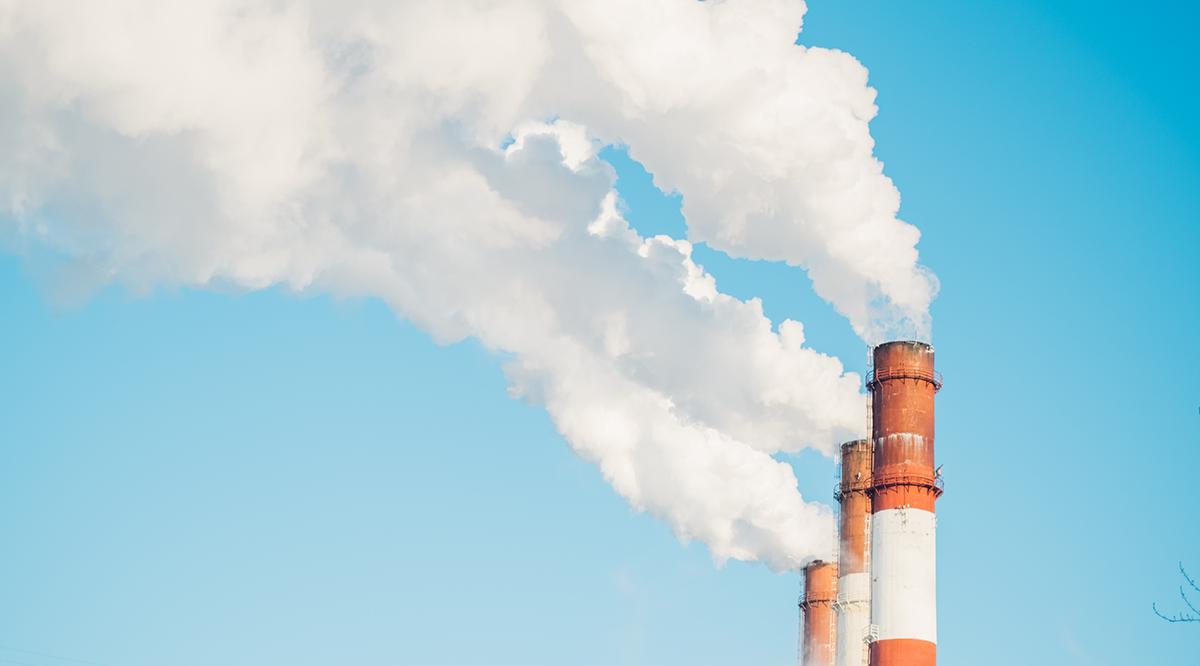 Steam and smoke billows from smokestack at massive thermal power plant on a clear blue sky background