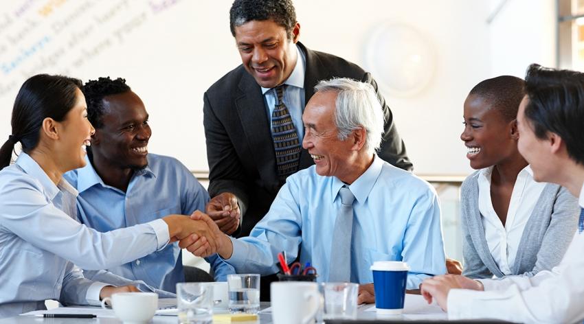 Business people sitting around table shaking hands during meeting