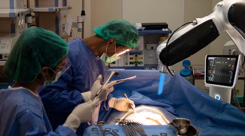 Doctors in blue scrubs and white masks performing surgering using robotic equipment