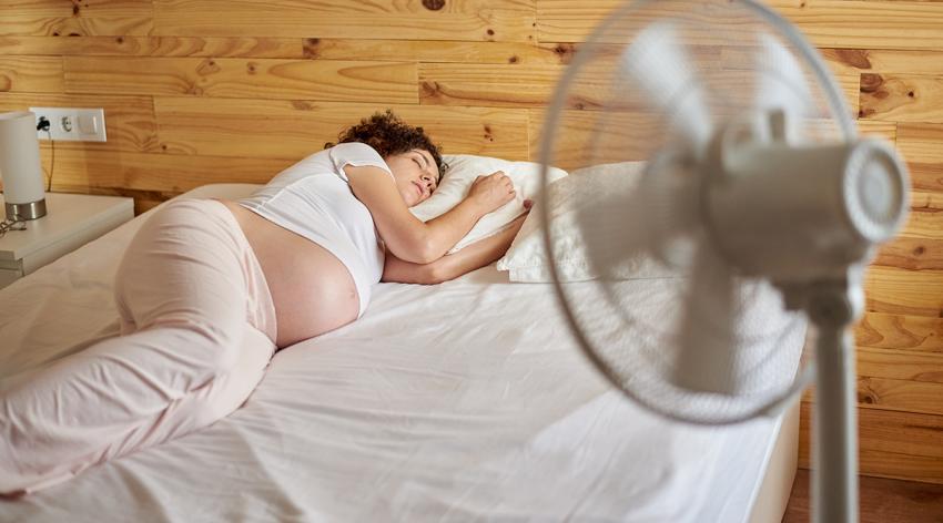 Pregnant woman in bed with a fan because of the heat wave