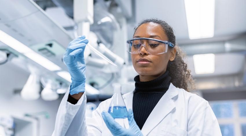 Woman scientist experimenting with chemicals in lab. Lab technician doing research on new chemicals in laboratory, adding solution in conical flask.